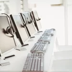 row of monitors and keyboards sitting on a desk
